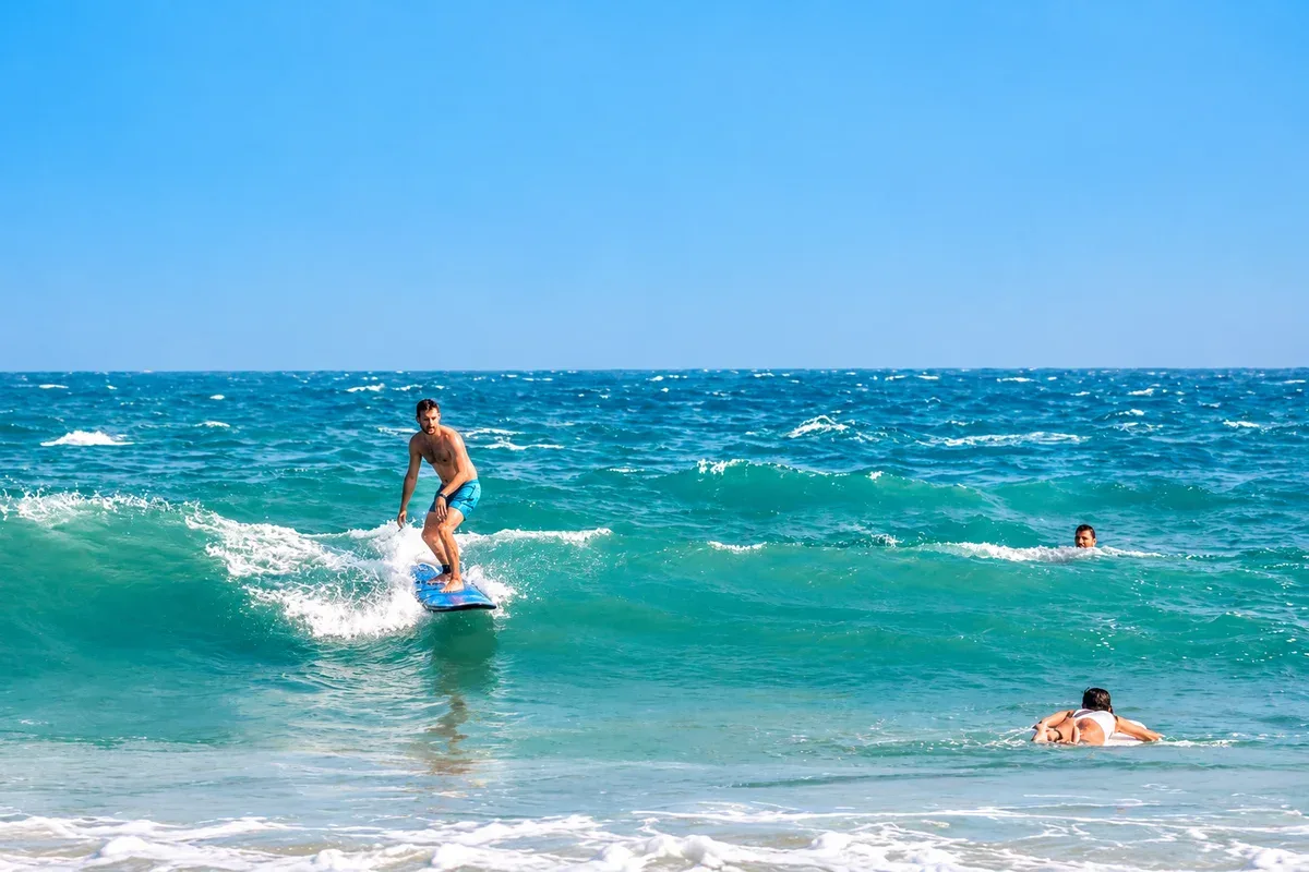 A surfer riding a small wave with other swimmers nearby