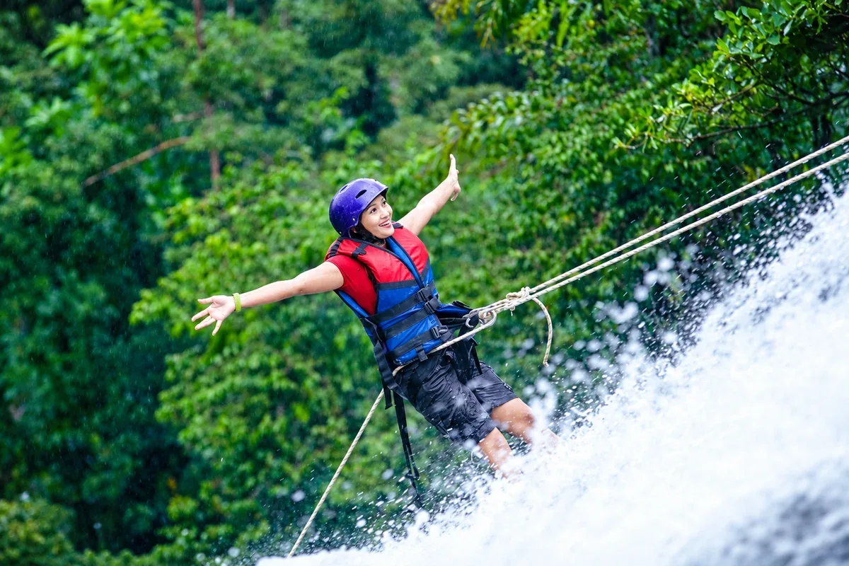 A visitor wearing a helmet and harness abseiling beside a waterfall