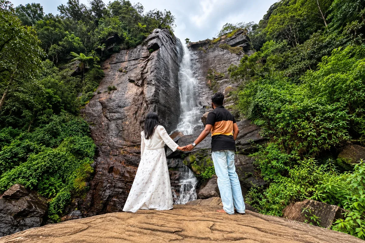 A couple standing beside a waterfall surrounded by forest near Nuwara Eliya