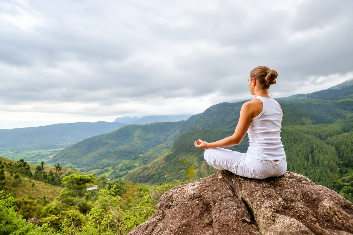 A woman meditating on a rock overlooking a misty green valley
