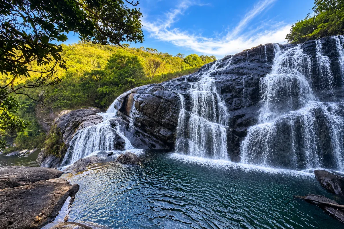 Water cascading over broad rocks into a pool surrounded by forest