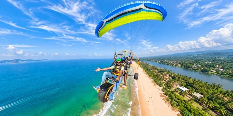 Two people enjoying a powered paraglider flight above a tropical coastline