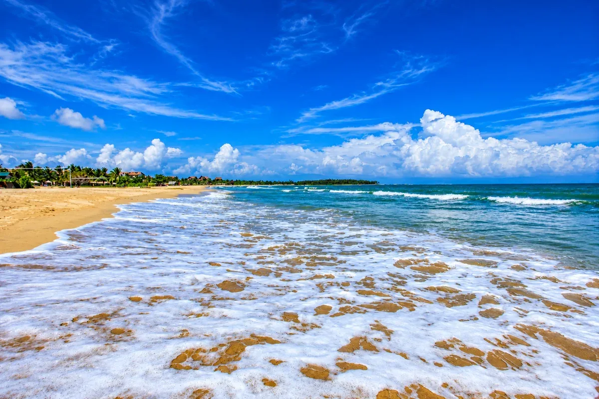 Gentle waves washing onto a wide sandy beach beneath a blue sky